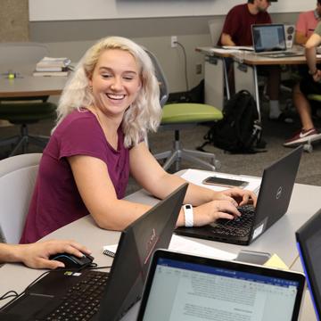 一个学生微笑着瞥了一眼另一个学生的电脑屏幕.